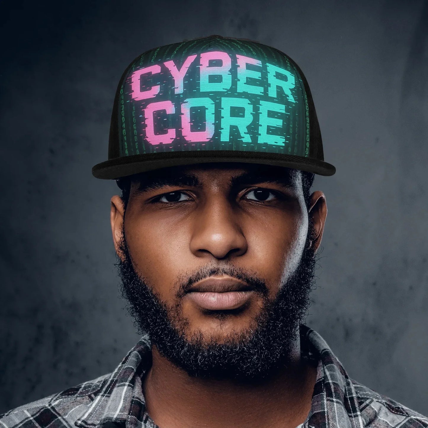 Headshot of a man wearing a black "Cyber Core" baseball cap and a plaid shirt against a dark gray background.