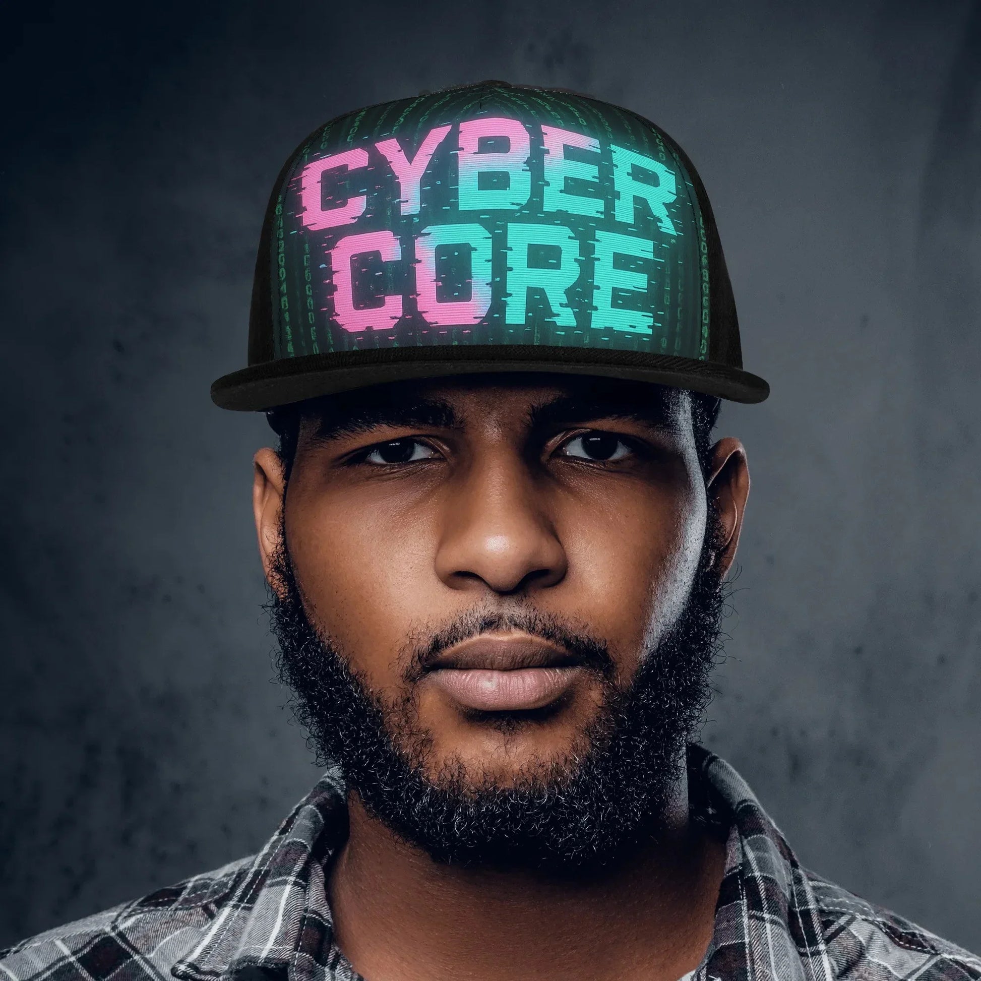 Headshot of a man wearing a black "Cyber Core" baseball cap and a plaid shirt against a dark gray background.